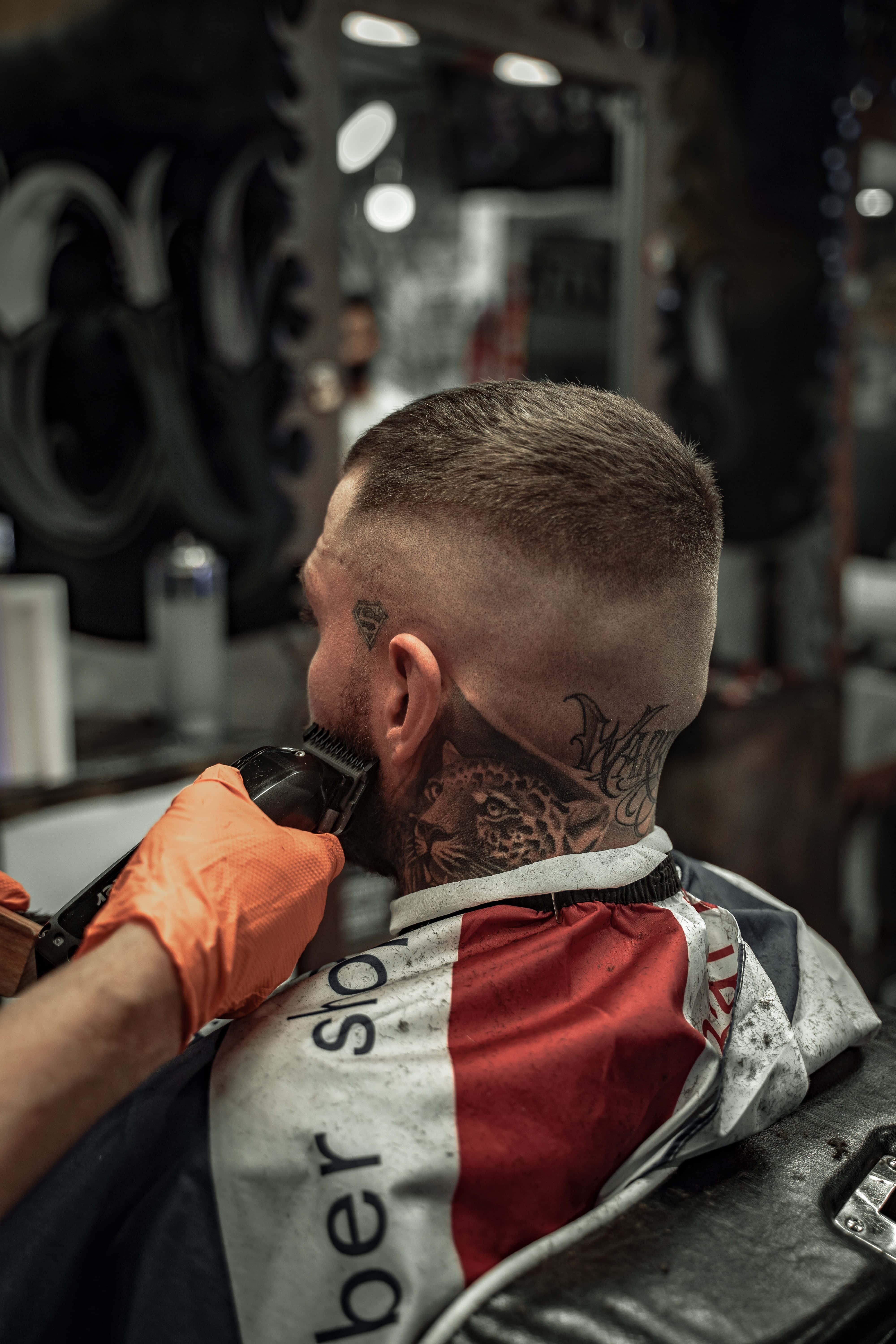 Barber 桌布 壁紙 — 一名頸上有豹紋紋身的男子，在理髮店穿著紅白斗篷理髮。