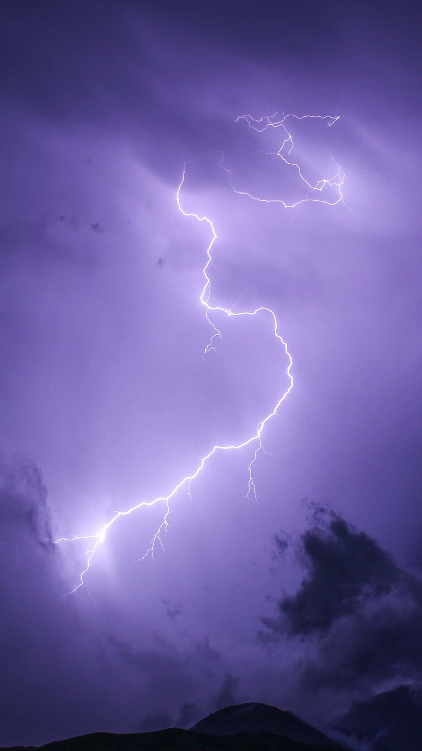 Lightning iPhone 桌布 壁紙 — 一道明亮的白色閃電在深紫色暴風雨天空中分叉，下方是黑暗的山脈輪廓。