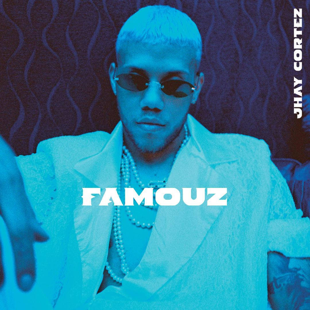 Jhay Cortez《Famouz》專輯封面 壁紙 — 一名頭髮漂白、戴著太陽眼鏡的男子，身穿白色西裝，佩戴珍珠項鍊，背景為有紋理的藍色。