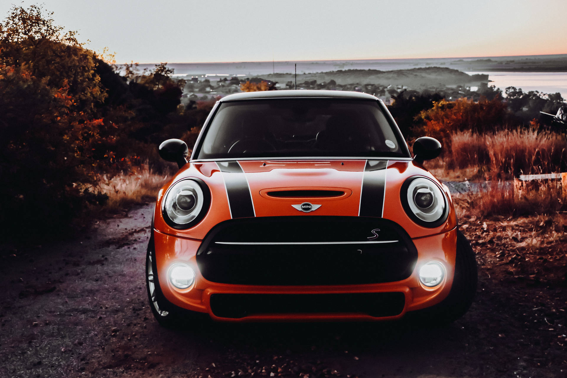 橙色MINI Cooper S停在日落時分的土路上，享有海岸景色和秋樹。