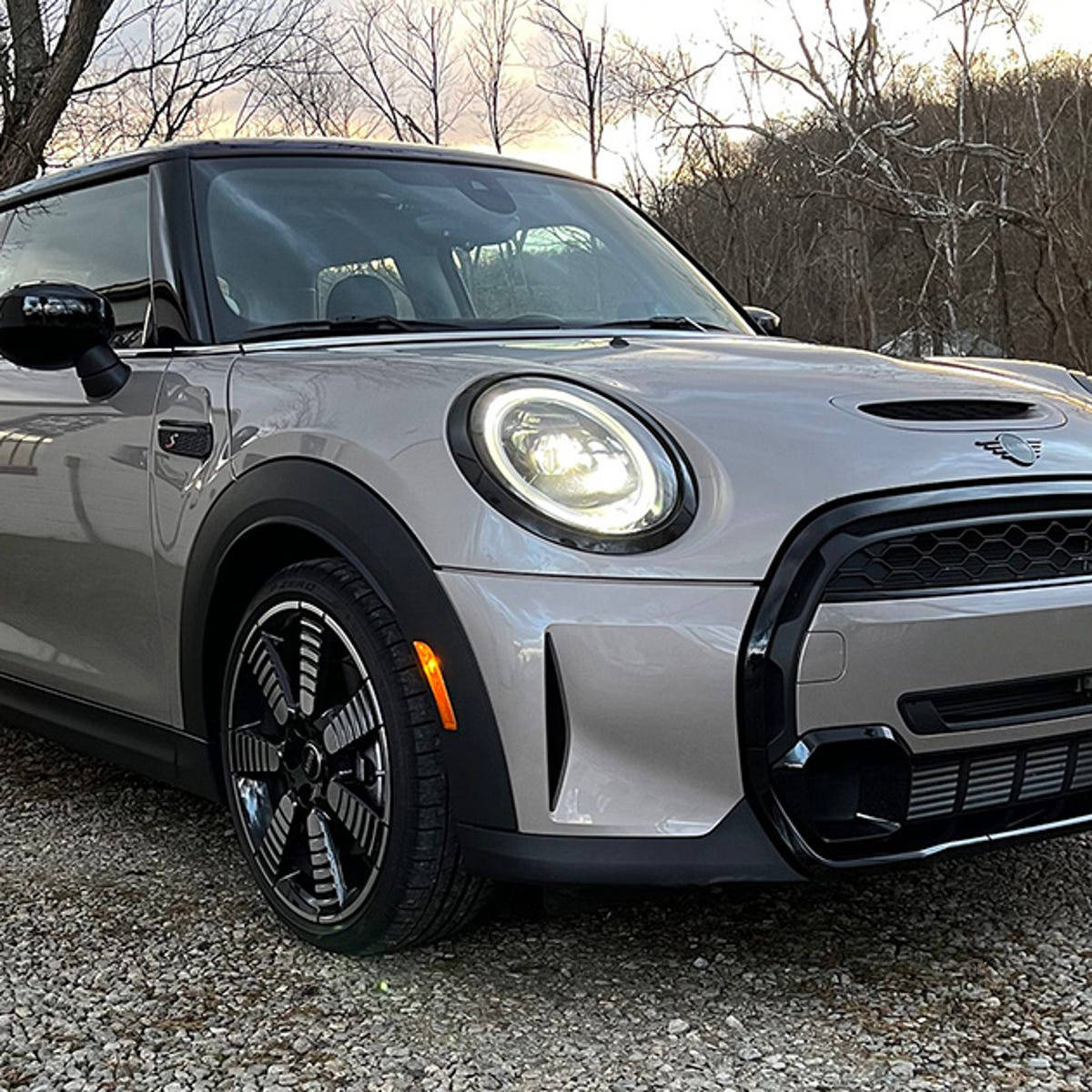 Mini 灰色美學車款 壁紙 — 一架時尚的銀色MINI Cooper停泊在碎石上，背景有光禿的樹木和柔和的金色光線。