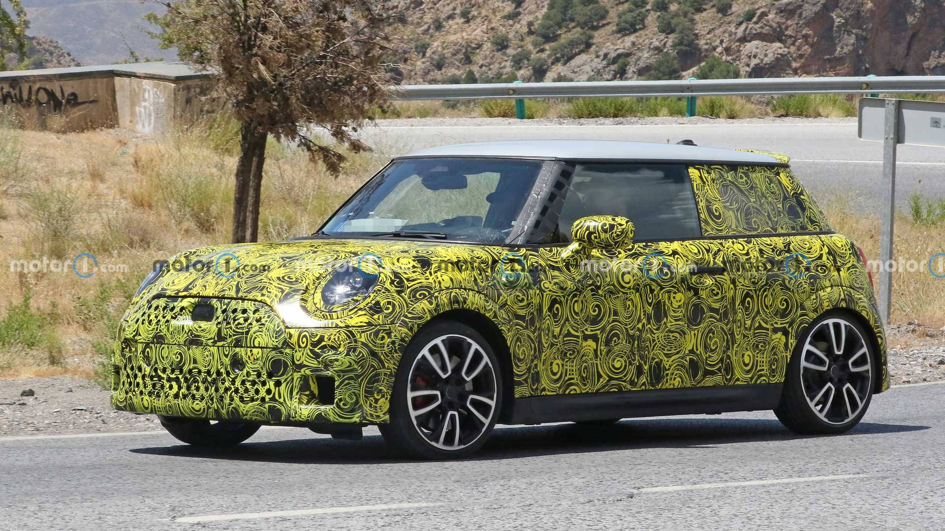 Mini 霓虹綠色迷幻塗裝 壁紙 — 一輛黃黑迷彩包裹的Mini Cooper原型車在陽光明媚的鄉村道路上行駛，背景有乾草和山丘。