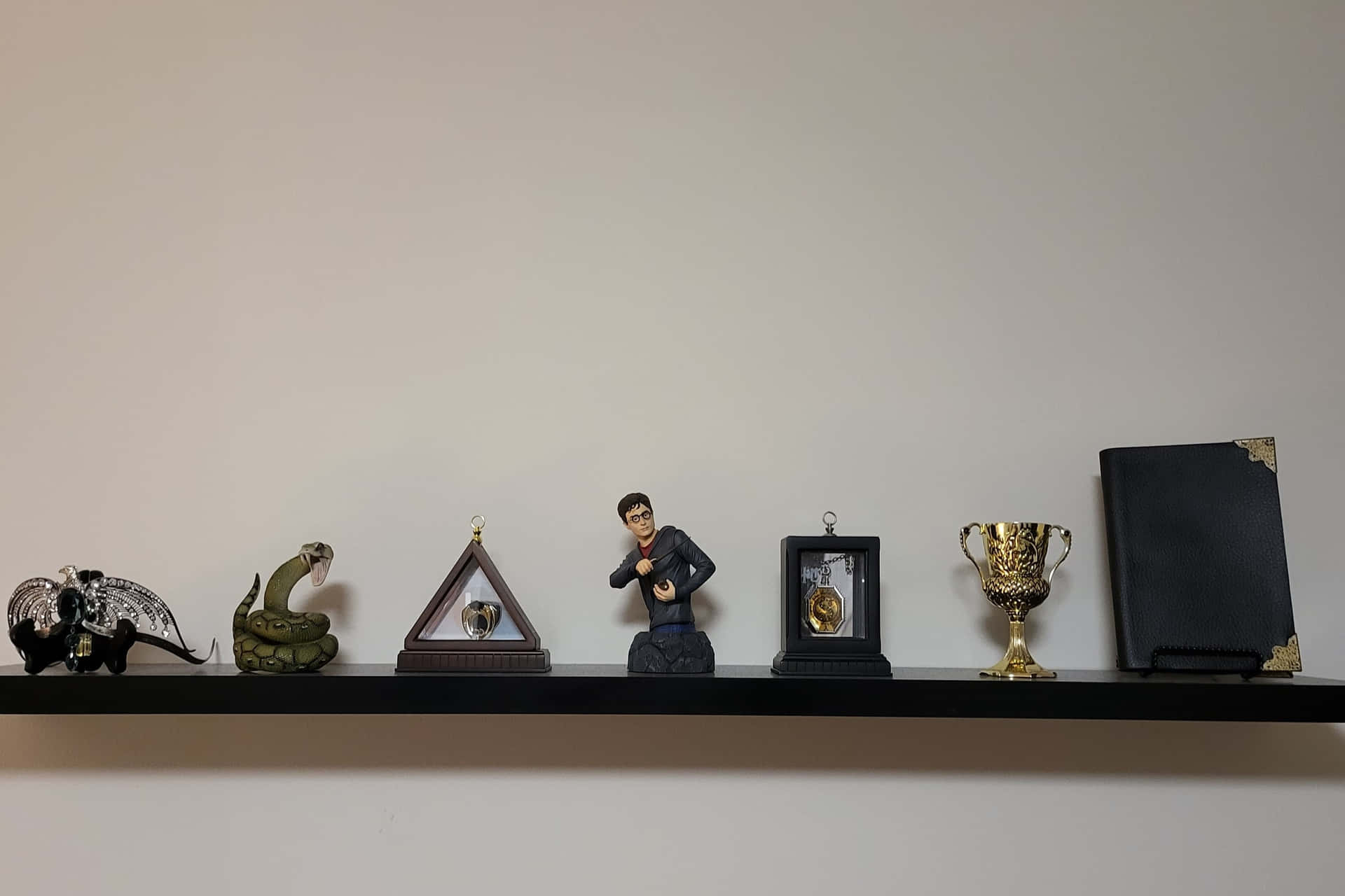  壁紙 — 一個簡約的架子上展示一排收藏品，包括蛇形公仔、獎盃和一個裱框肖像，背景是素牆。