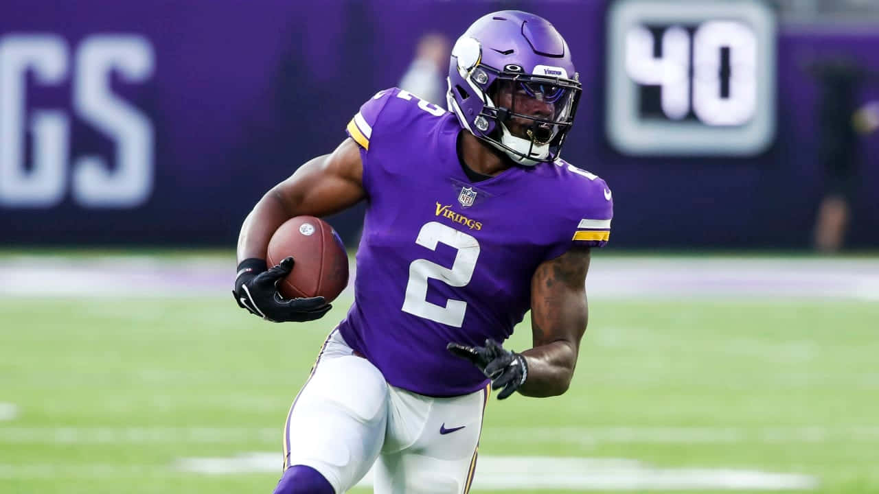  壁紙 — 一名身穿紫色球衣、背號二號的明尼蘇達維京人美式足球員在綠色球場上帶球衝刺。
