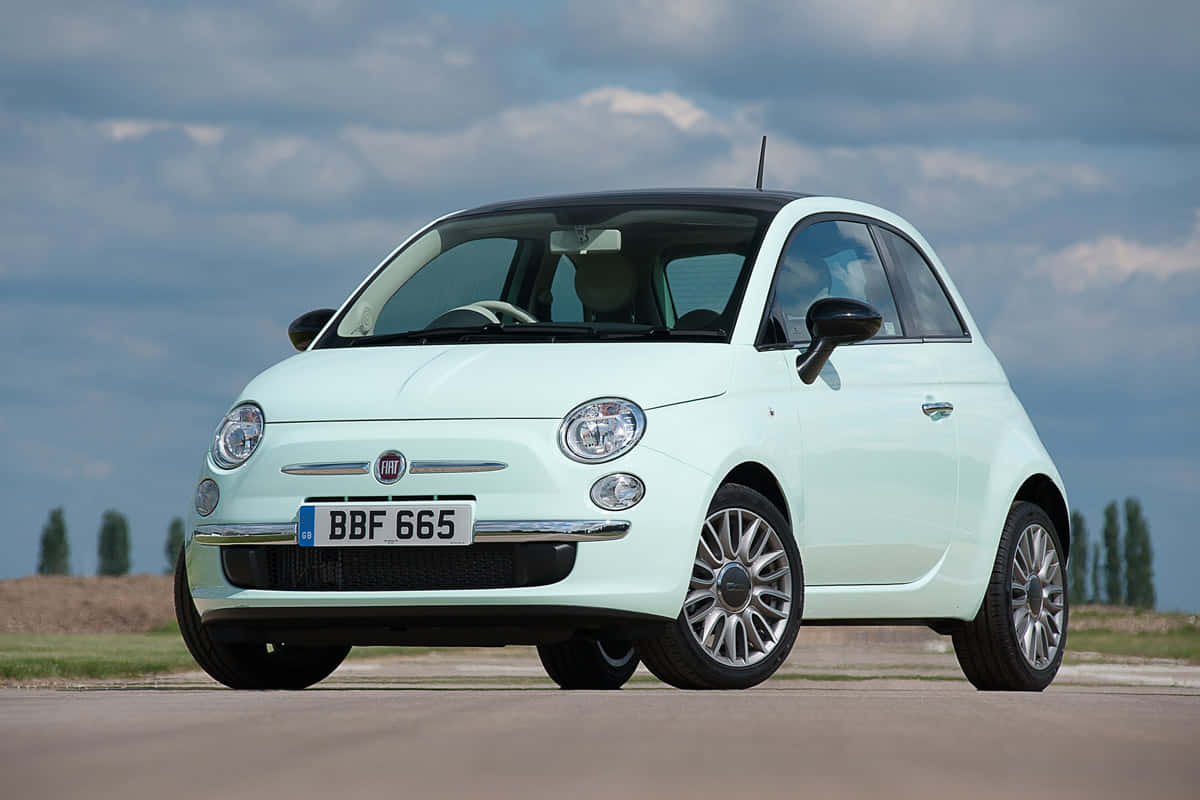 Fiat 500 桌布 壁紙 — 一架薄荷綠色嘅Fiat 500停泊喺一條開闊嘅道路上，天空多雲，遠處有樹木。
