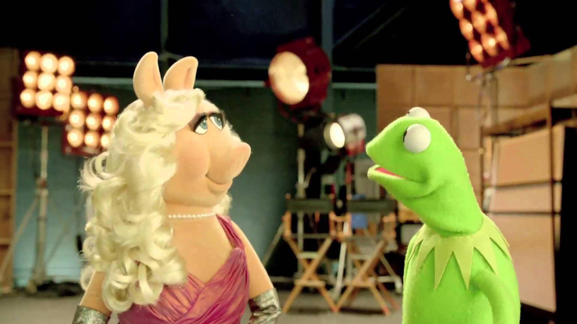 Miss Piggy 與 Kermit 蛙 壁紙 — 豬小姐和青蛙柯米特在溫暖照明的後台工作室中面對面，可見燈光設備和導演椅。