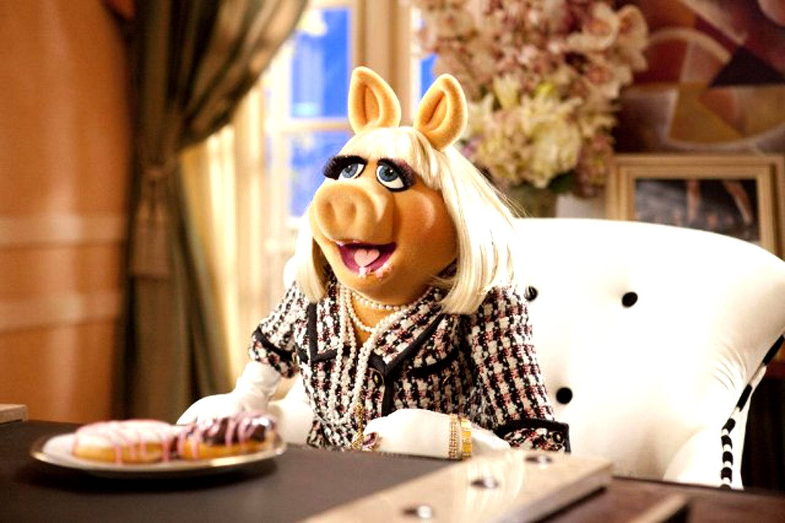 Miss Piggy 高級餐廳用餐 壁紙 — 豬小姐優雅地坐在白色椅子上，穿著時尚的黑白格紋西裝，佩戴珍珠，微笑著看著一盤甜甜圈。