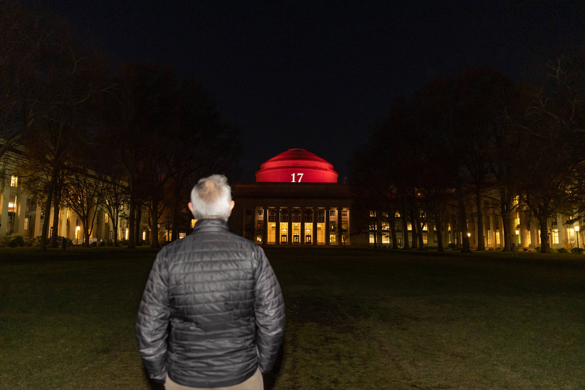 一個穿著黑色外套的男人夜晚站在草地上，看著一座帶有紅色圓頂並標有17的建築。