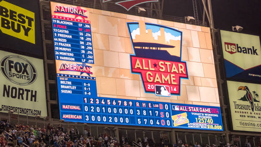 MLB比分：國家聯盟對美國聯盟 壁紙 — 一個巨大的照明記分牌在擠滿人的棒球場上，在明亮的球場燈光下顯示2014年MLB全明星賽的比分和球員統計數據。