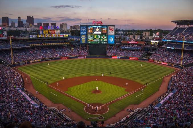 MLB比分：特納球場觀眾席 壁紙 — 一個充滿活力的棒球場在黃昏時分，色彩繽紛的暮色天空下擠滿了歡呼的球迷。