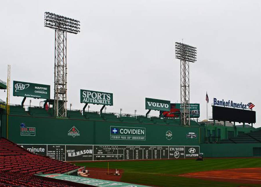 MLB比分：空無一人的球場 壁紙 — 在灰色天空下，一個陰天在棒球場，有綠色外野牆、紅色座位和高聳的泛光燈。