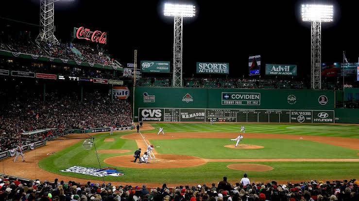 MLB比分：芬威球場比賽 壁紙 — 夜晚擠滿人的棒球場，明亮的燈光照亮球場，投手向打者投球，觀眾歡呼聲震天。