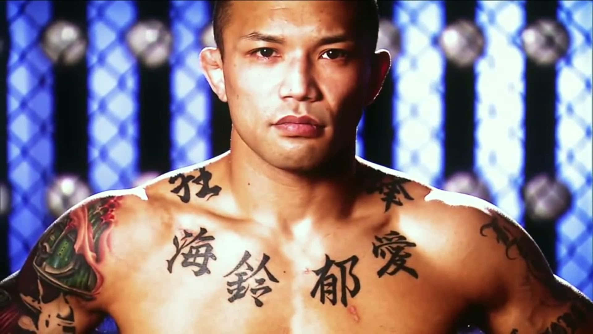 日本職業MMA選手山本信一郎中景照 壁紙 — 一個肌肉發達的戰士，胸前紋有中文字，在藍色鐵絲網背景下凝視著。