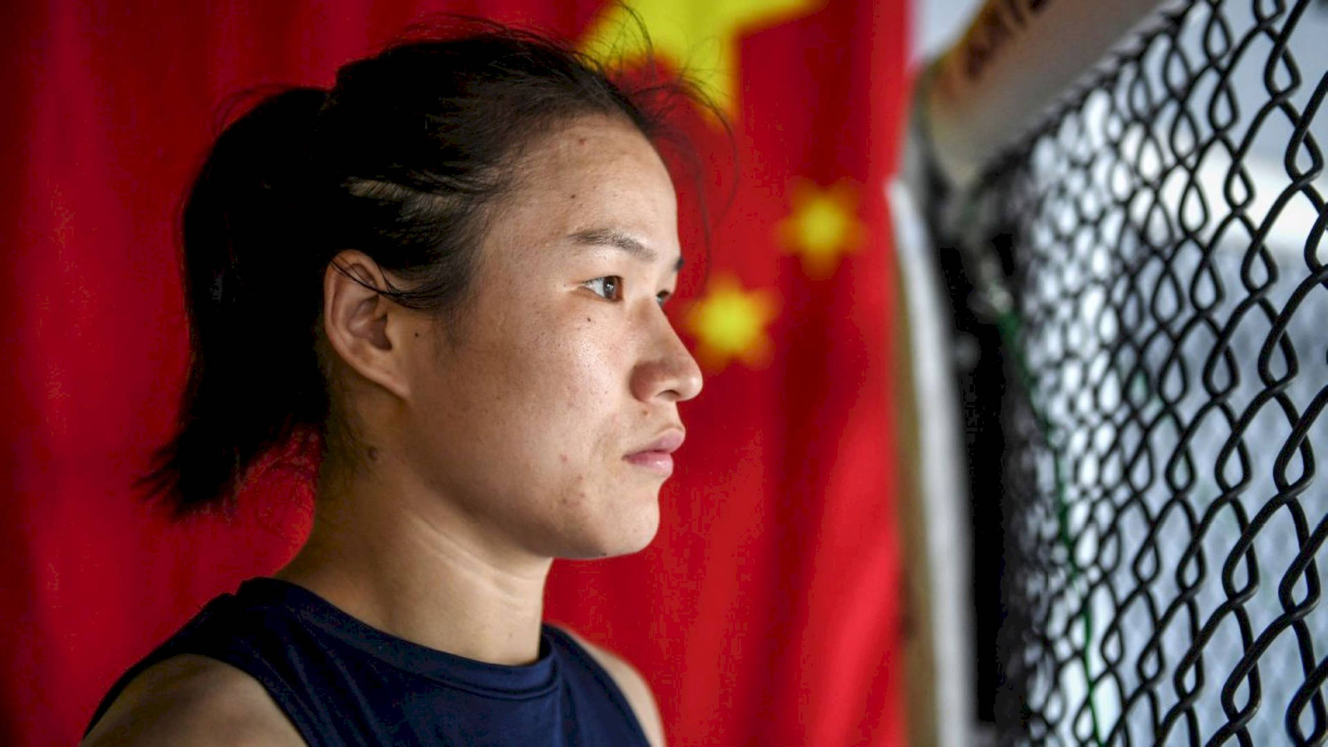 一位堅定的女戰士透過圍欄觀望，背景有中國國旗。