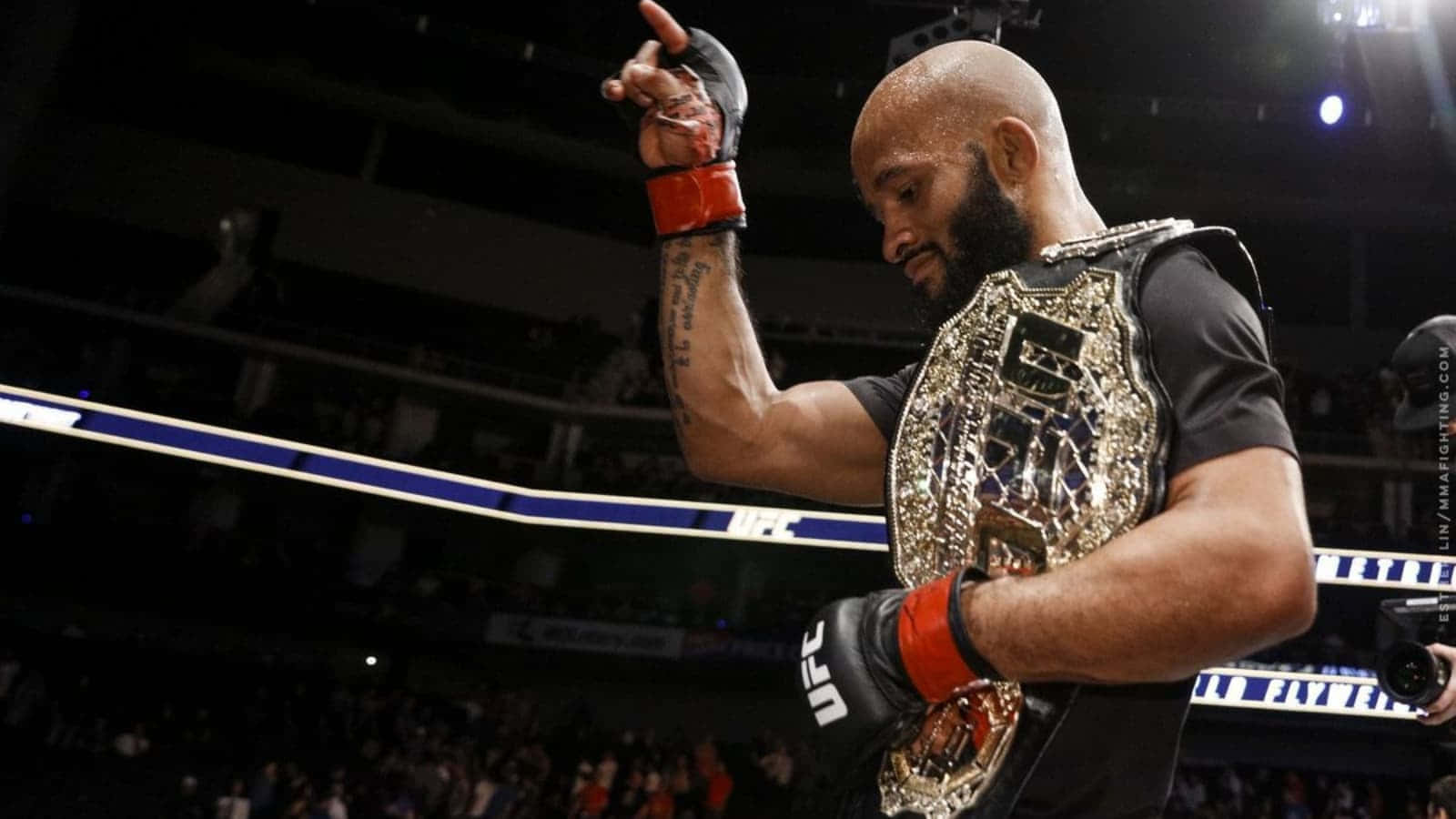 MMA冠軍德米特里烏斯·約翰遜化身「強力鼠」 壁紙 — 一位勝利嘅UFC拳手帶住冠軍腰帶，喺八角籠內嘅場館燈光下高舉佢嘅手套手慶祝勝利。
