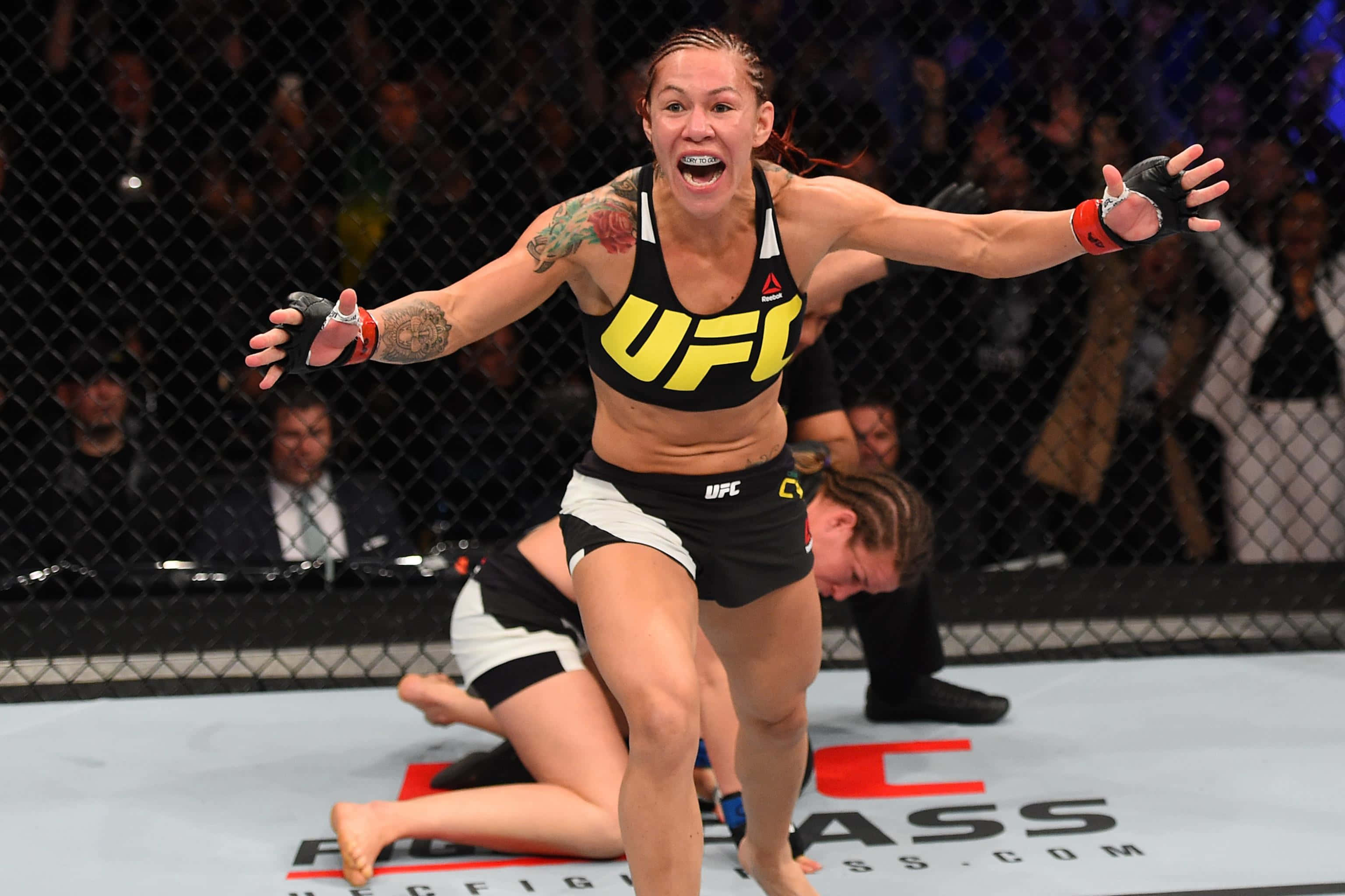 MMA選手Cris Cyborg 2016賽事慶祝照 壁紙 — 一位女性UFC拳手在八角籠中張開雙臂，發出勝利的吶喊慶祝勝利。