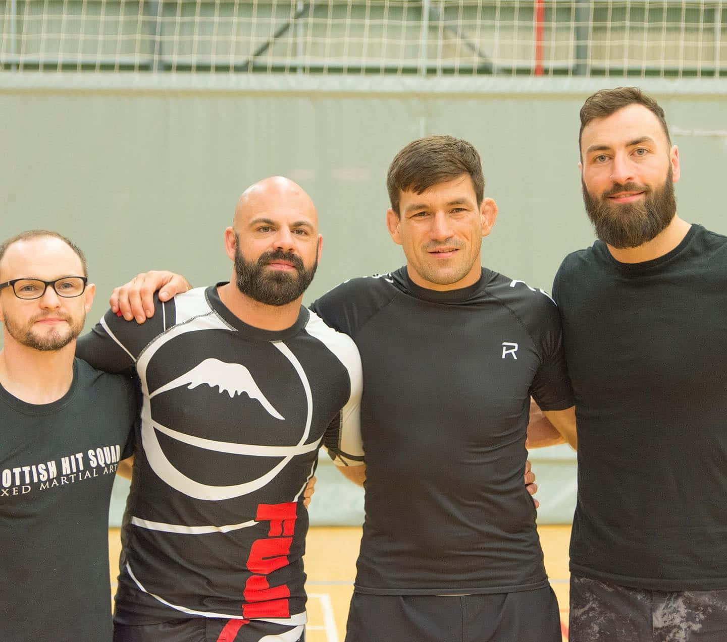 MMA選手保羅·克雷格與隊友合影 壁紙 — 四位留鬍鬚嘅男士穿著武術裝備，喺體育館內自信地擺姿勢，手臂互相搭喺對方身上。