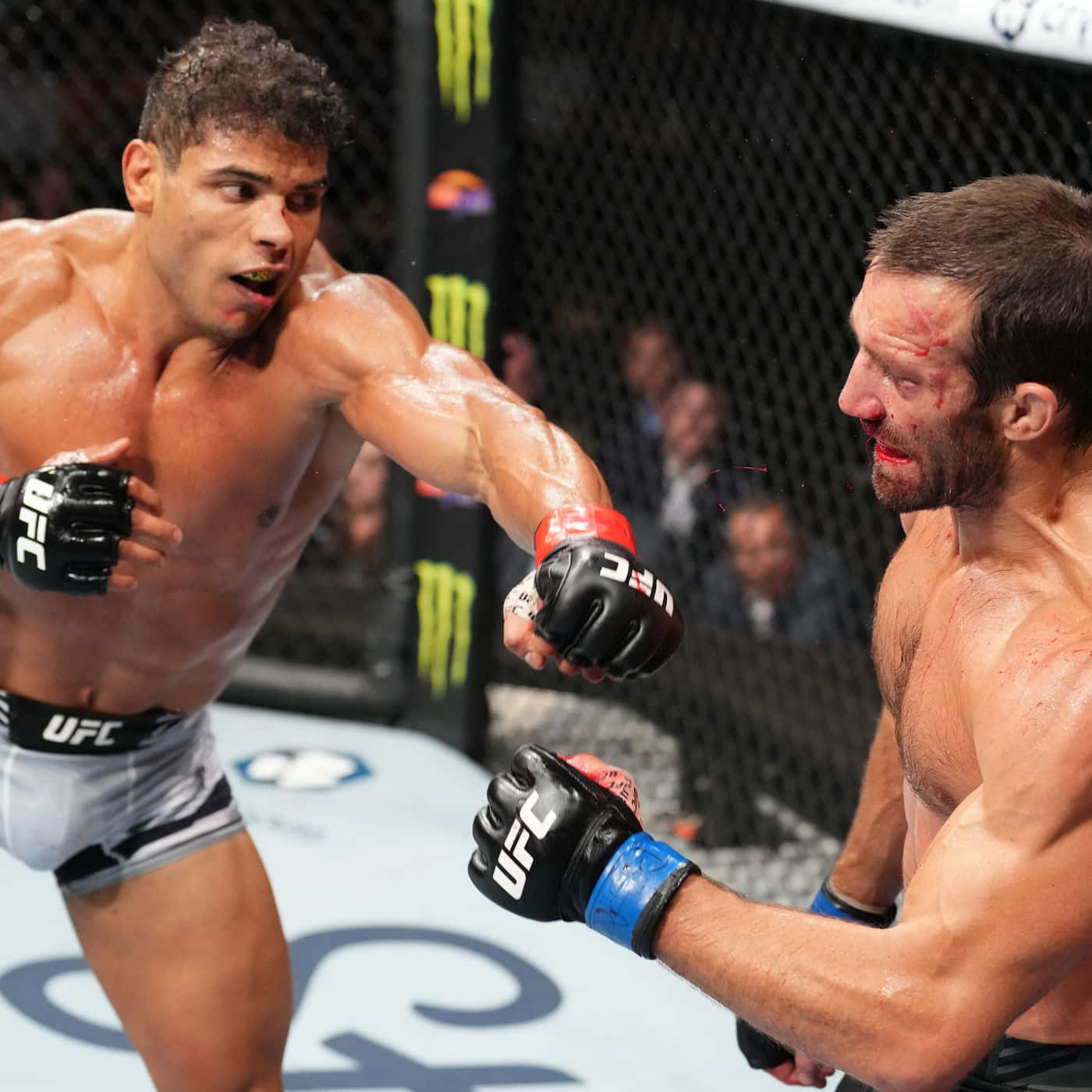 MMA選手保羅·科斯塔與盧克·羅克霍德UFC 278賽事 壁紙 — 兩名MMA拳手在激烈的籠中賽中交鋒，滿臉鮮血，汗水在明亮的場館燈光下閃閃發光。