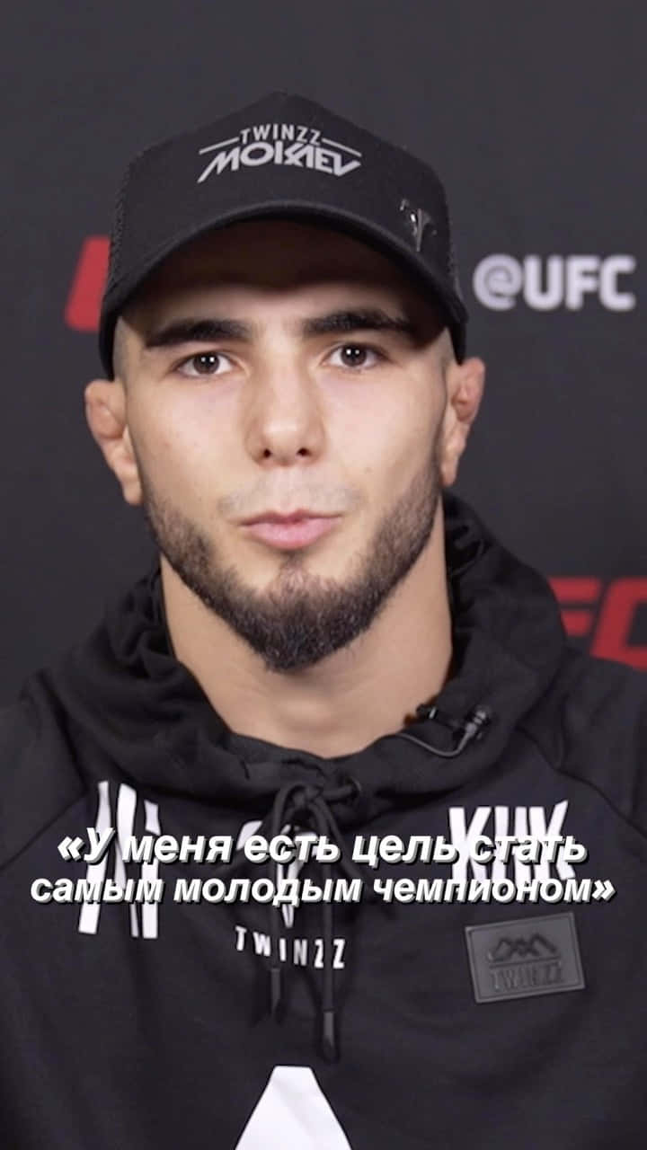 年輕男性運動員在UFC活動中戴黑色鴨舌帽和連帽衫，帶有俄語引文疊加。
