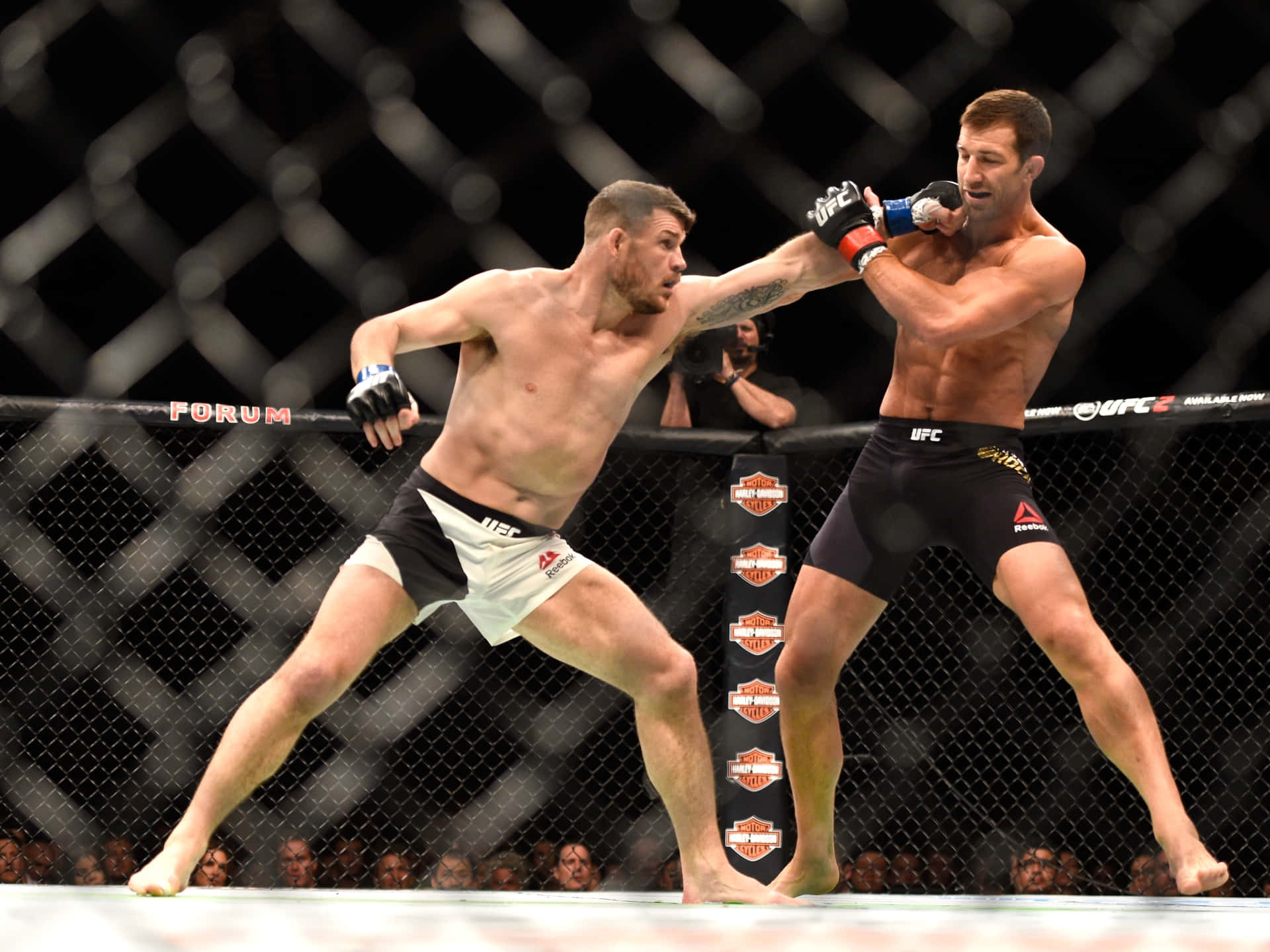 MMA選手邁克爾·比斯平與盧克·羅克霍德對戰 壁紙 — 兩名肌肉發達的MMA拳手在籠中交鋒，其中一人揮拳，觀眾專注觀看。
