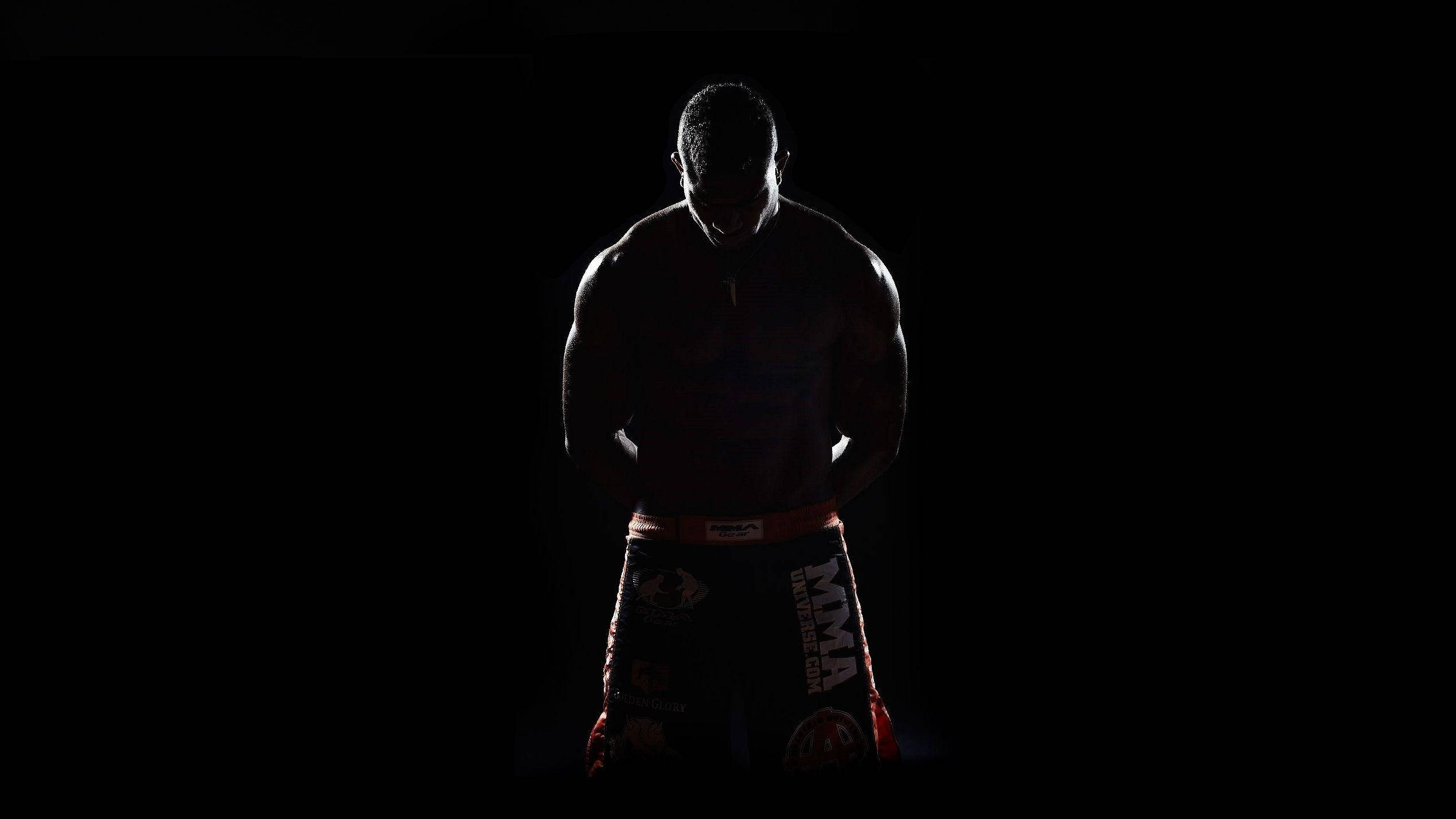 MMA陰影中的阿利斯泰爾·奧弗埃姆 壁紙 — 一位肌肉發達的MMA拳手以剪影姿態站在黑色背景前，短褲帶有微弱的紅色飾邊。