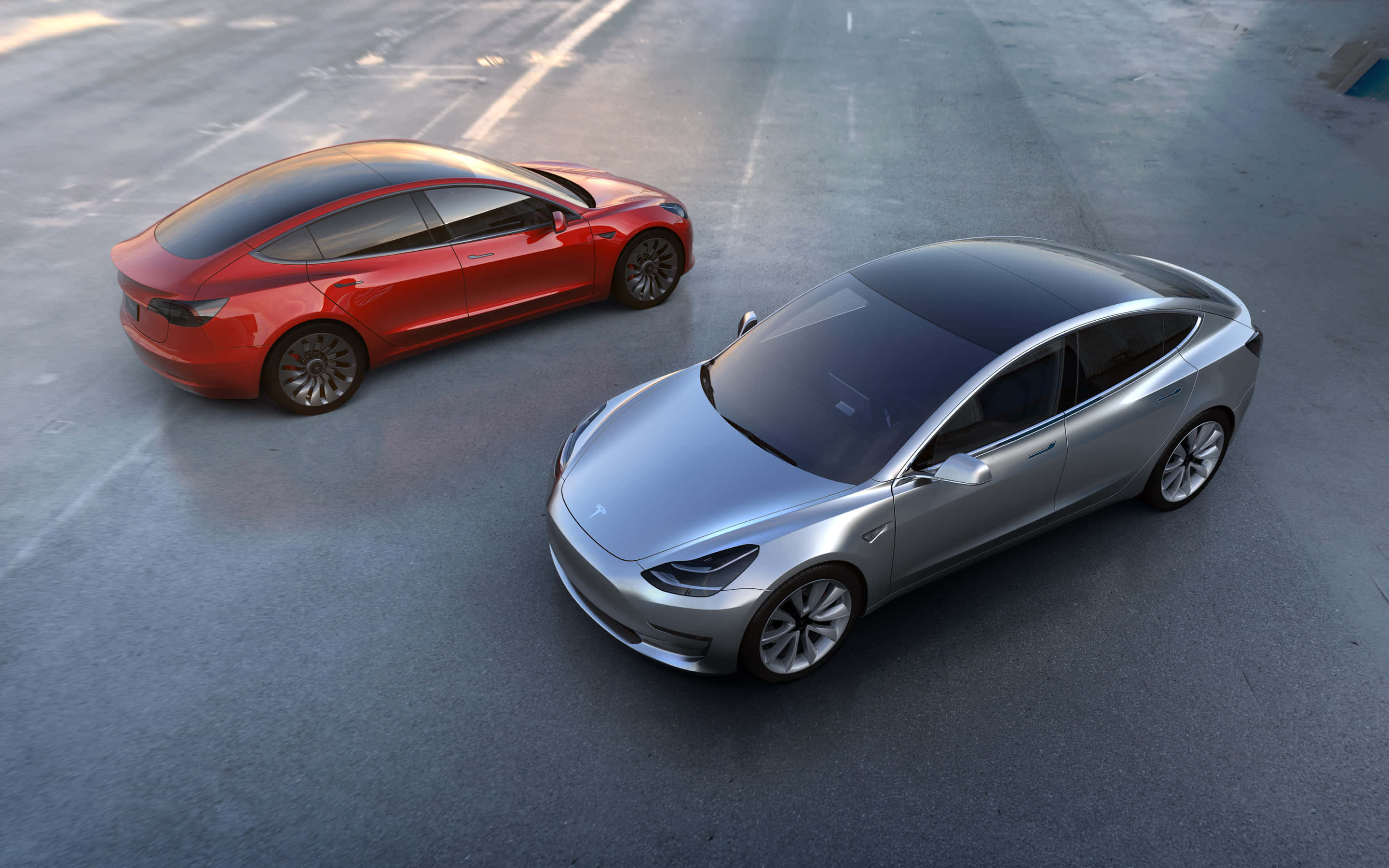 體驗特斯拉 Model 3 的力量 壁紙 — 兩輛流線型Tesla Model 3房車，一紅一銀，停泊在混凝土停車場，柔和日光下。