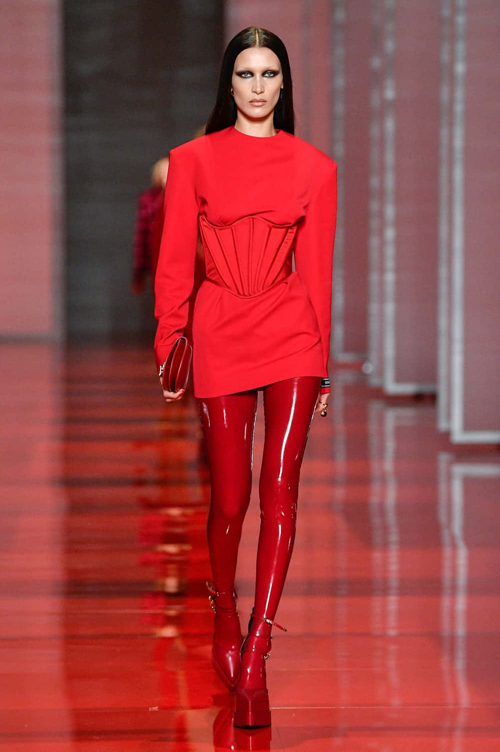 Red Clothing 桌布 壁紙 — 一位模特兒自信地走在光亮的紅色天橋上，身穿大膽的紅色束腰連衣裙和相配的閃亮緊身褲。