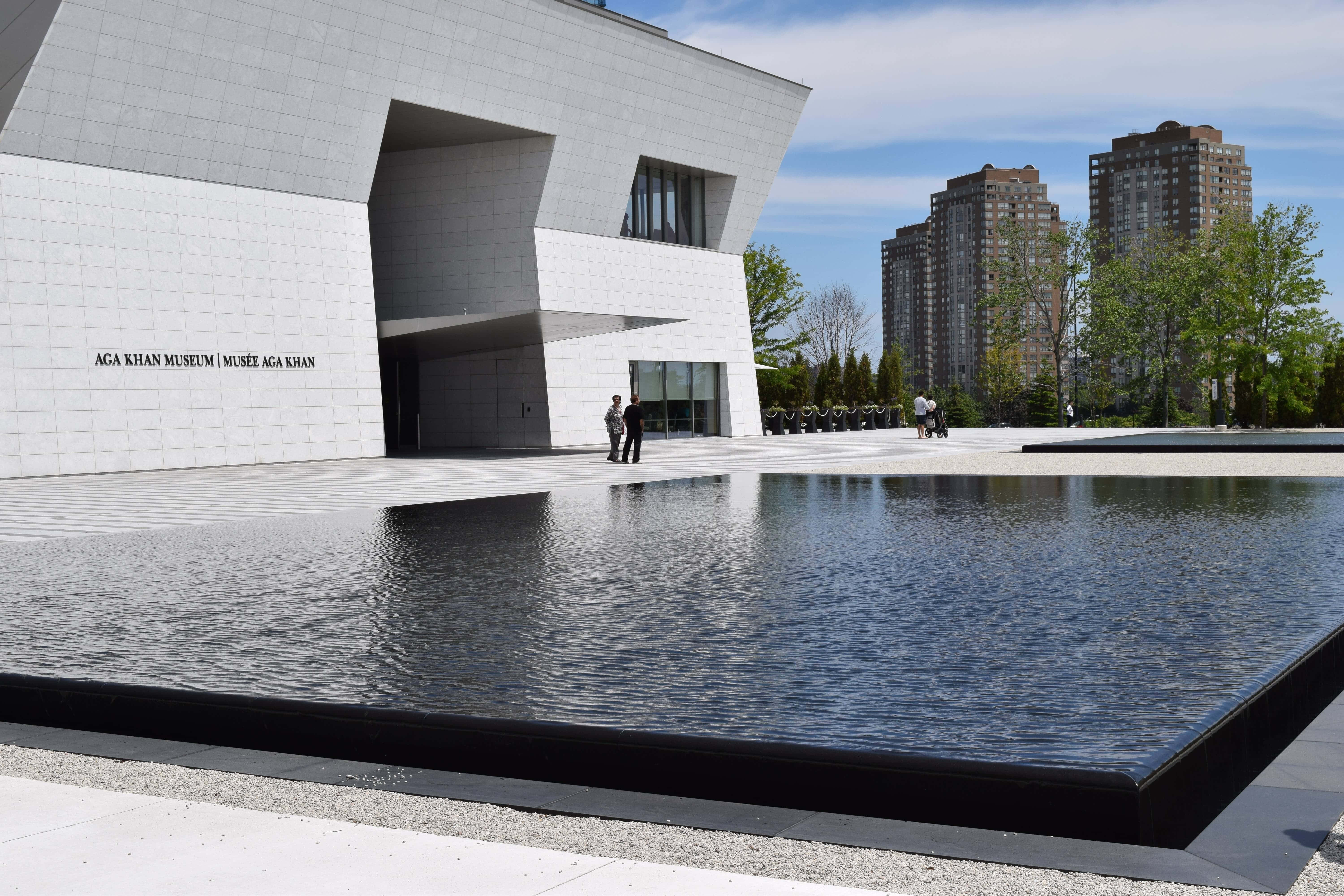 Aga Khan Museum 桌布 壁紙 — 現代白色石頭博物館，幾何建築倒映在平靜的水景中，上方是明亮的藍天。