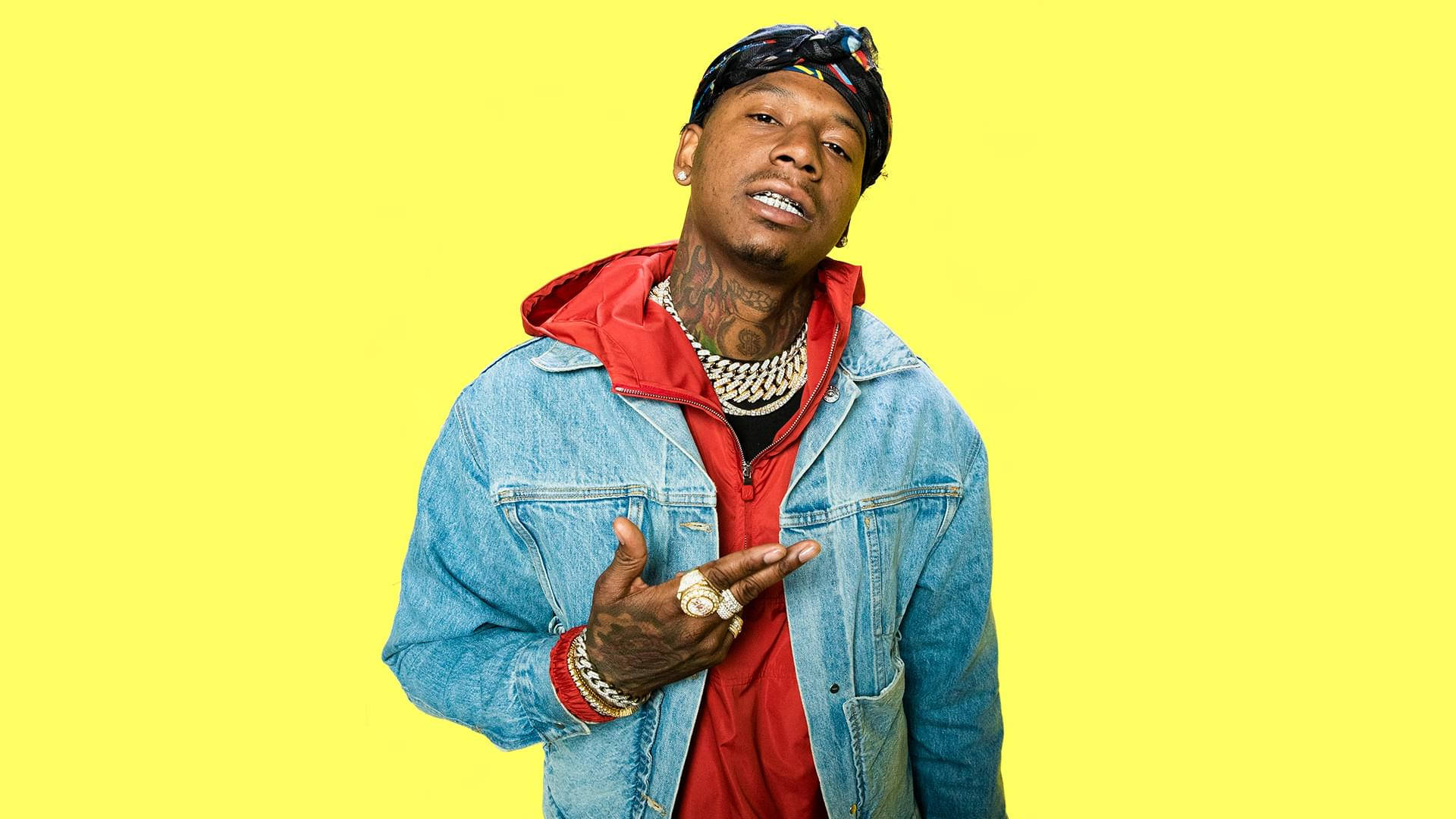 Moneybagg Yo 肖像照 壁紙 — 一個穿著牛仔外套和紅色連帽衫的男人在明亮的黃色背景前自信地擺姿勢。