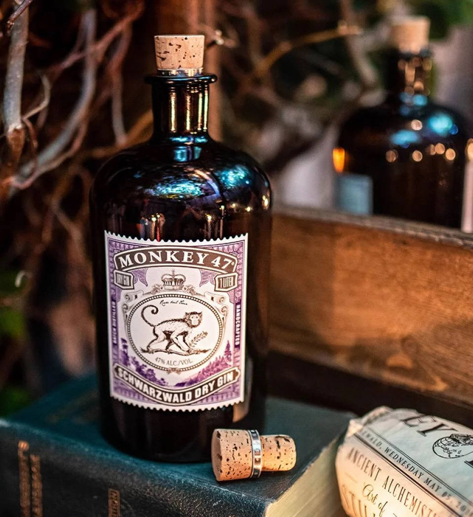 Monkey 47黑森林乾金酒 — 德國烈酒 壁紙 — 一個深藍色的Monkey 47氈酒瓶連軟木塞放在復古書籍上，旁邊有另一個瓶子和一本名為Ancient Alchemist的書。