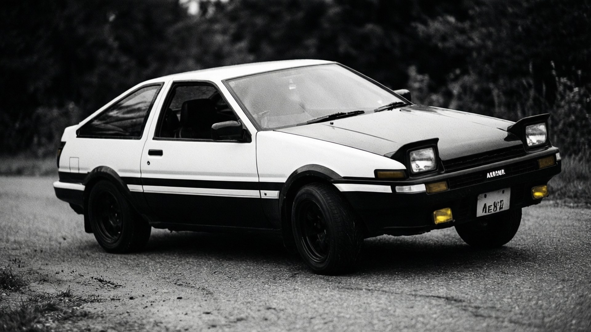 黑白豐田AE86 Corolla Levin停泊在碎石路上，後面有樹木