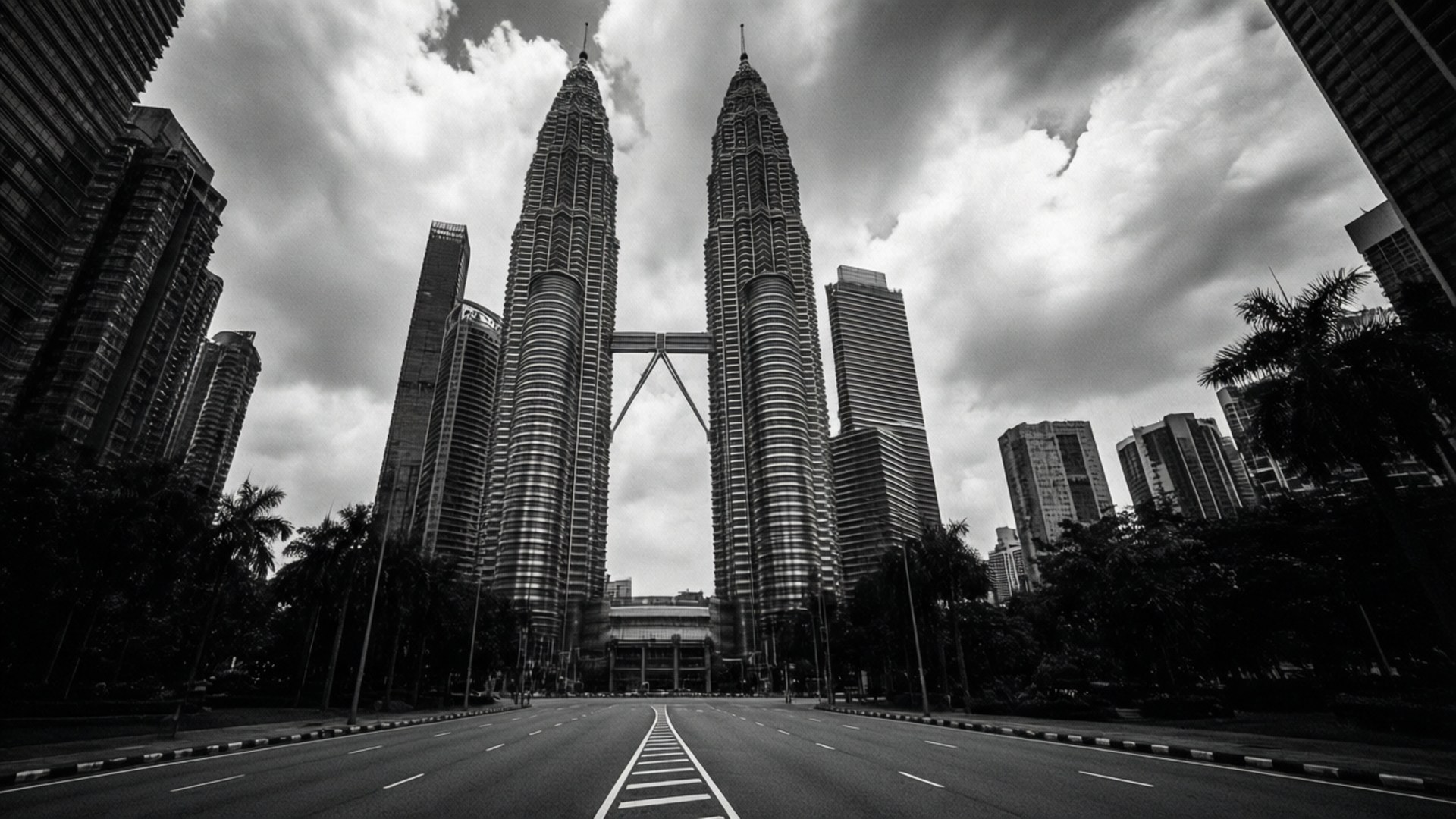 Monochrome Giants 壁紙 — 一張戲劇性的低角度黑白照片，展示雙子塔被寬闊空蕩的道路和陰天天空所環繞。