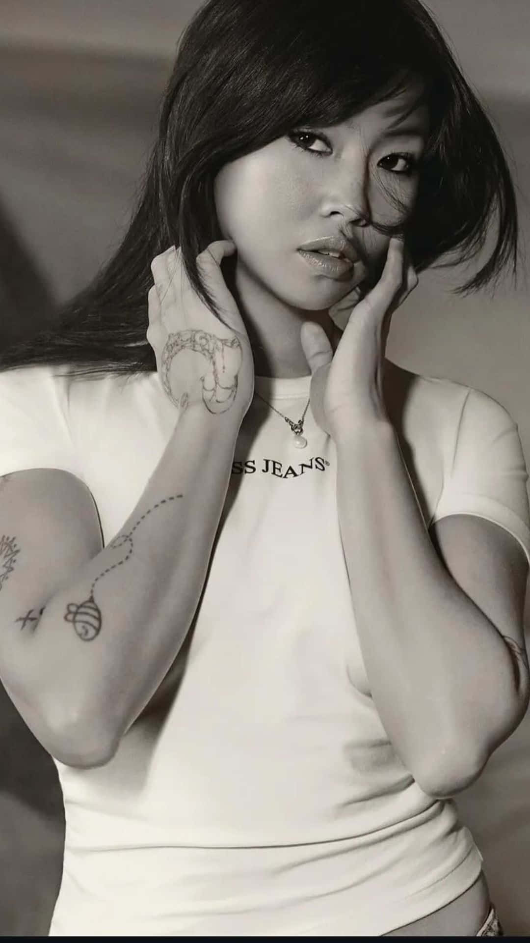  壁紙 — 一位手臂和手上有紋身的女性黑白肖像，身穿白色T恤，以沉思的表情直視鏡頭。