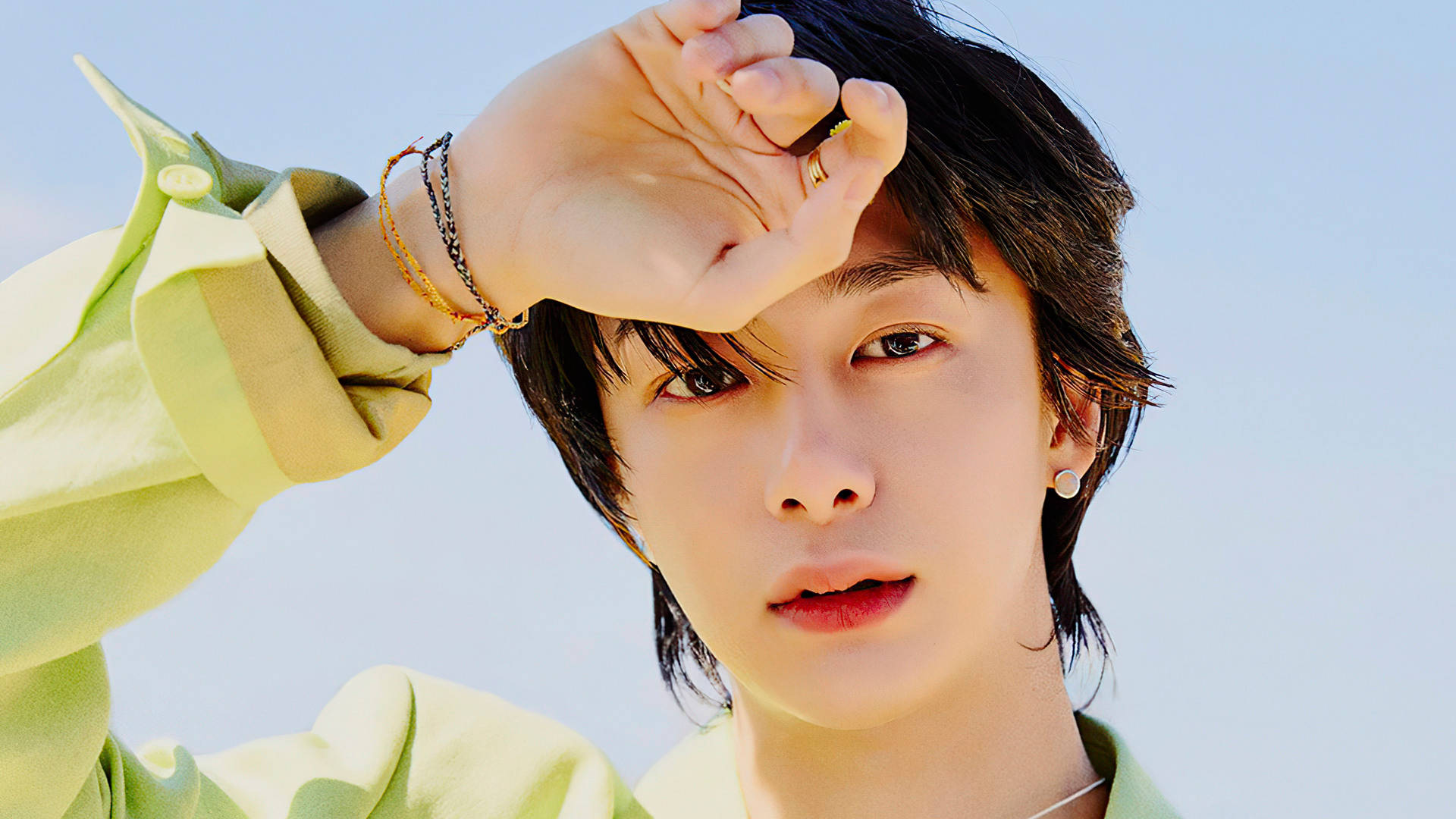 Monsta X Hyungwon 綠色上衣 壁紙 — 一位深色頭髮、穿著淺綠色襯衫的年輕人，在清澈的藍天下遮擋刺眼的陽光。