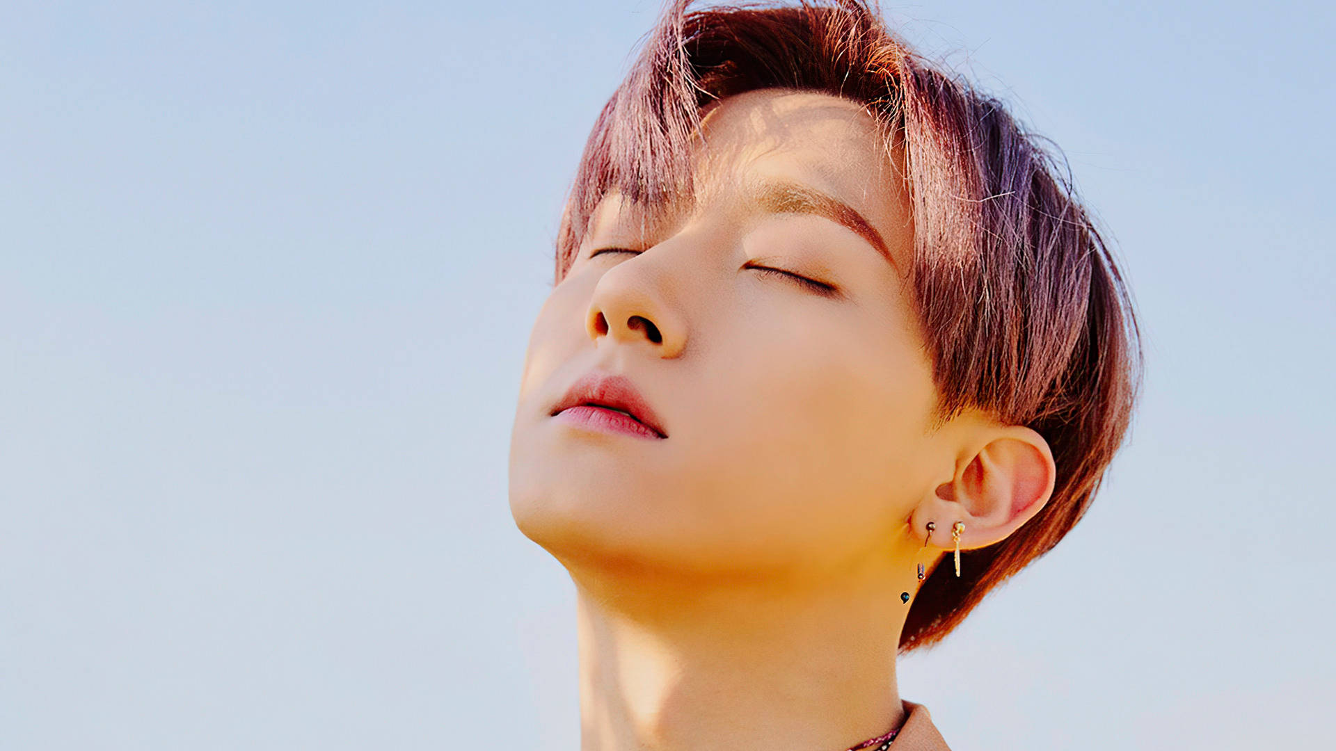 Monsta X IM 戶外拍攝 壁紙 — 一位短紫髮、閉眼的年輕人，頭向後靠在清澈的藍天上。