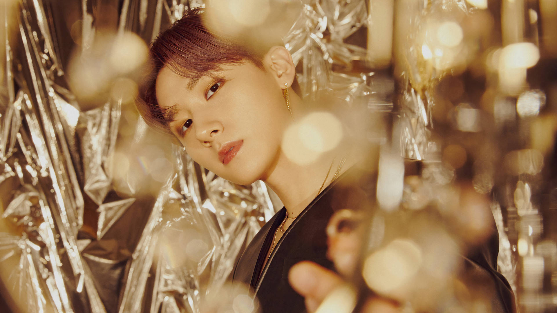 Monsta X IM 金色主題 壁紙 — 一個人溫柔地透過閃爍的金色箔紙凝視，周圍有散景燈光閃爍。