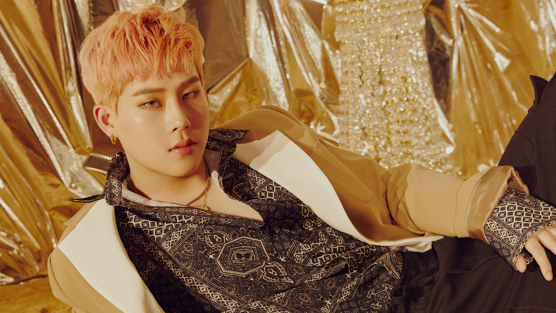 Monsta X Joohoney 金光閃閃 壁紙 — 一位年輕男子擁有蜜桃色頭髮，靠著閃爍的金色背景，穿著圖案黑白和米色服裝。