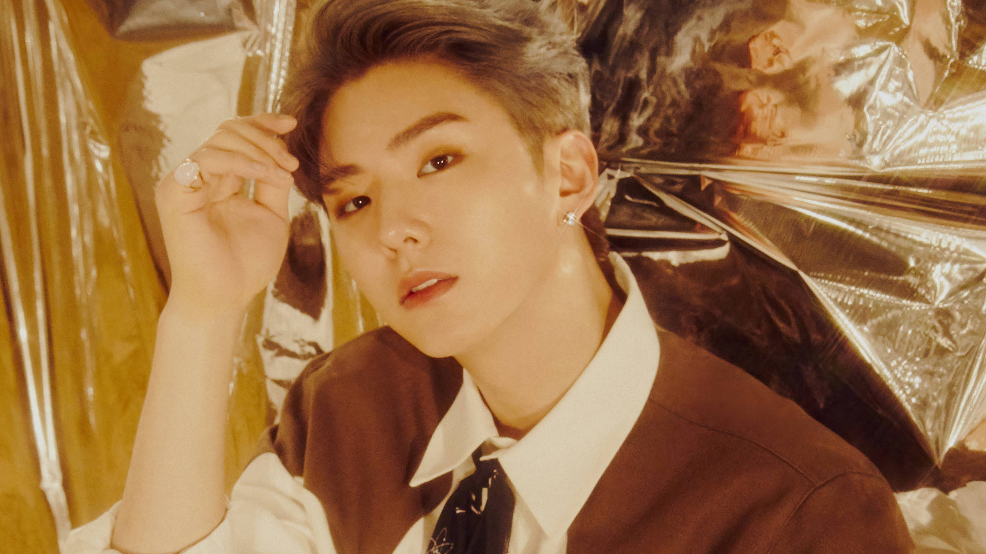 Monsta X Kihyun 金色主題 壁紙 — 一位年輕男子，擁有時尚髮型和珠寶飾品，在溫暖燈光下，以皺褶金箔背景擺姿勢。