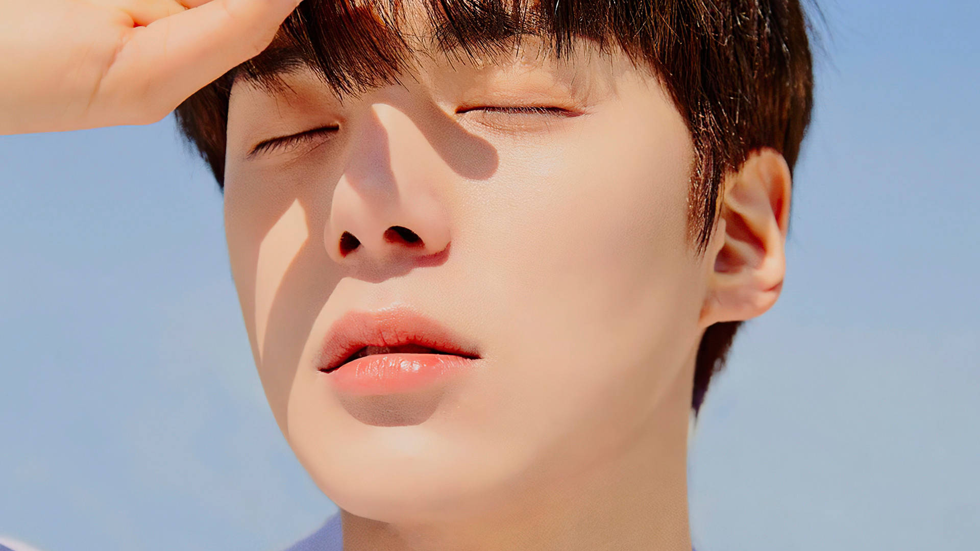 Monsta X Minhyuk 阳光遮眼 壁紙 — 一名年輕男子閉上眼睛，在晴朗的藍天下用手遮擋臉龐，沐浴在明亮的陽光中。