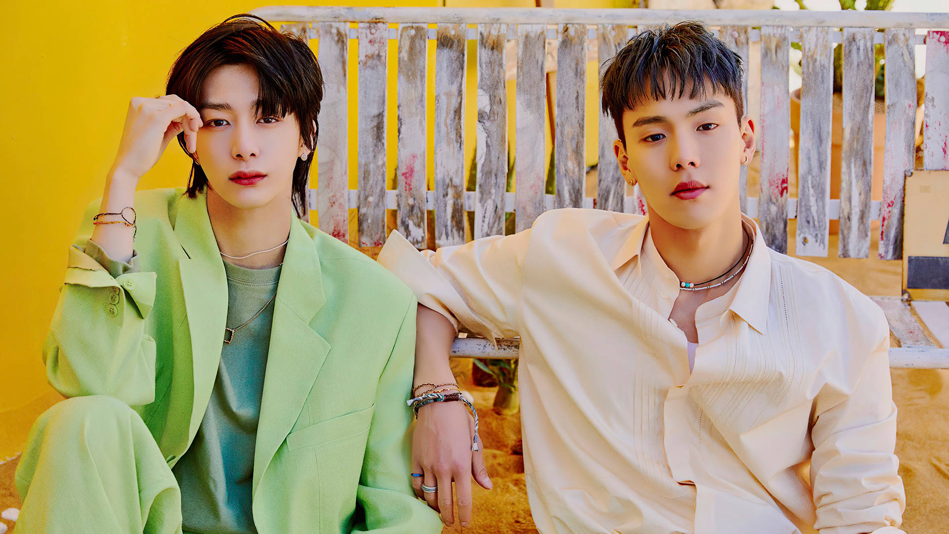 Monsta X Shownu 與 Hyungwon 壁紙 — 兩位時尚年輕男子自信地坐在一張風化的木長椅上，背景是一面充滿活力的黃色牆壁。
