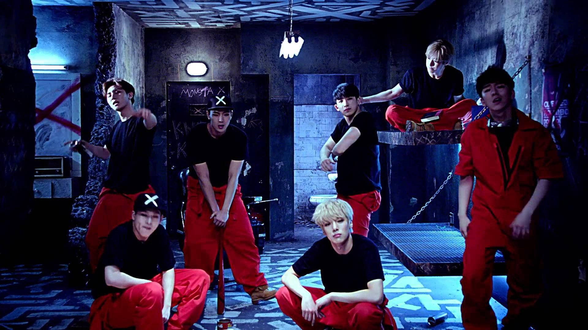 Monsta X Trespass 音樂影片 壁紙 — 七名身穿黑色上衣和紅色褲子的男性在一個帶有塗鴉和鏈條的粗糙藍色燈光地下房間中動態擺姿勢。
