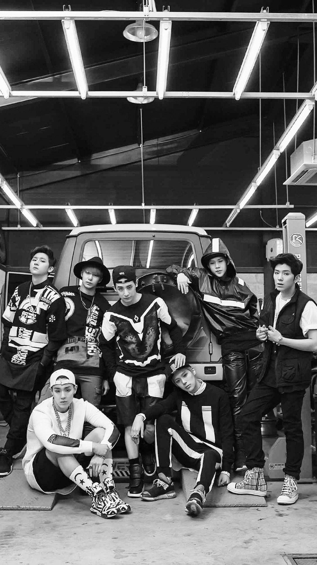 MONSTA X Trespass時期 壁紙 — 七位時尚年輕男子在粗糙的黑白車庫中，頭頂螢光燈，自信地擺出姿勢。