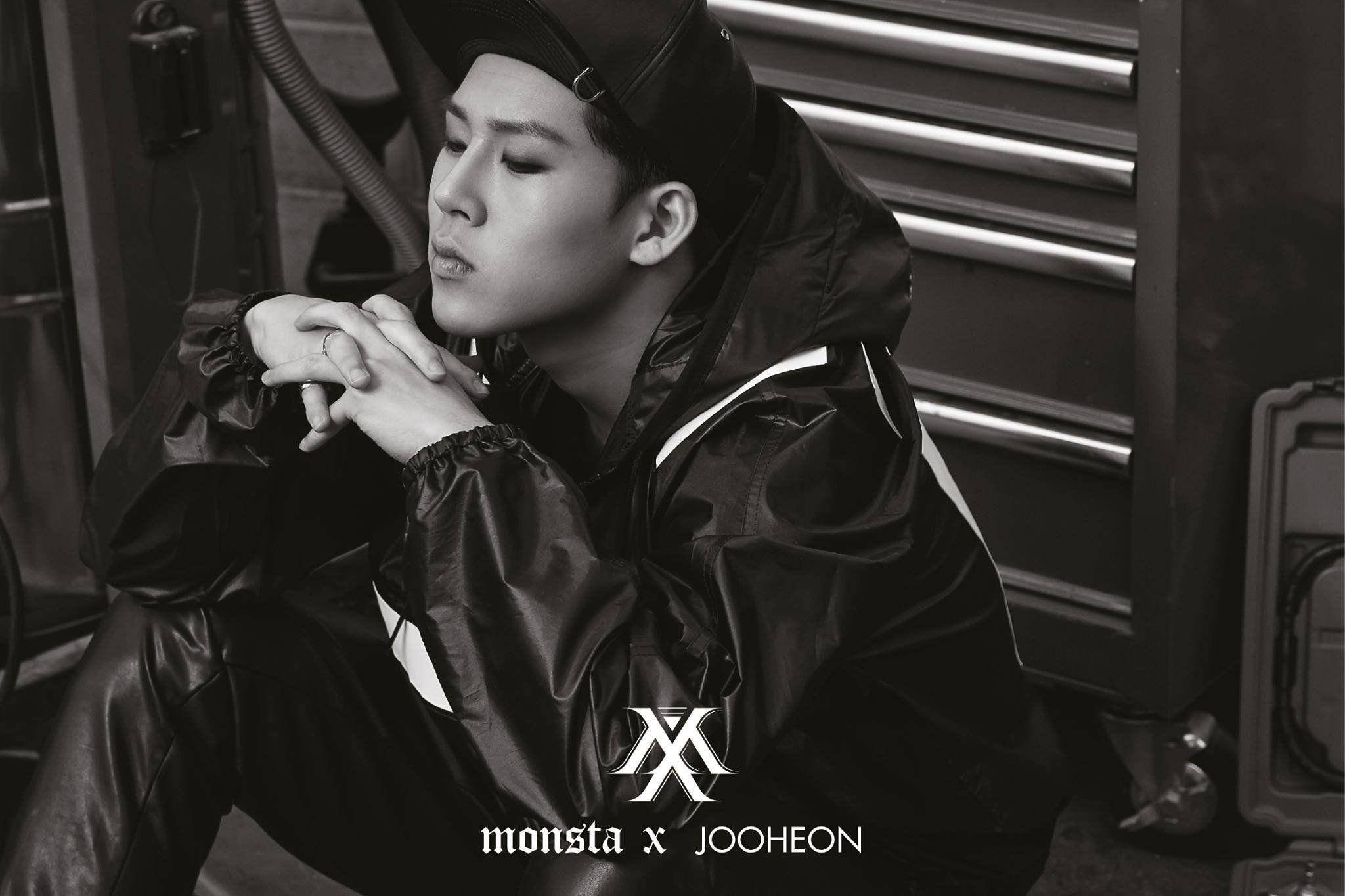 Monsta X 賈浩然 壁紙 — 一個身穿黑色外套和帽子的年輕男子，在單色調的車庫門前若有所思地坐著。