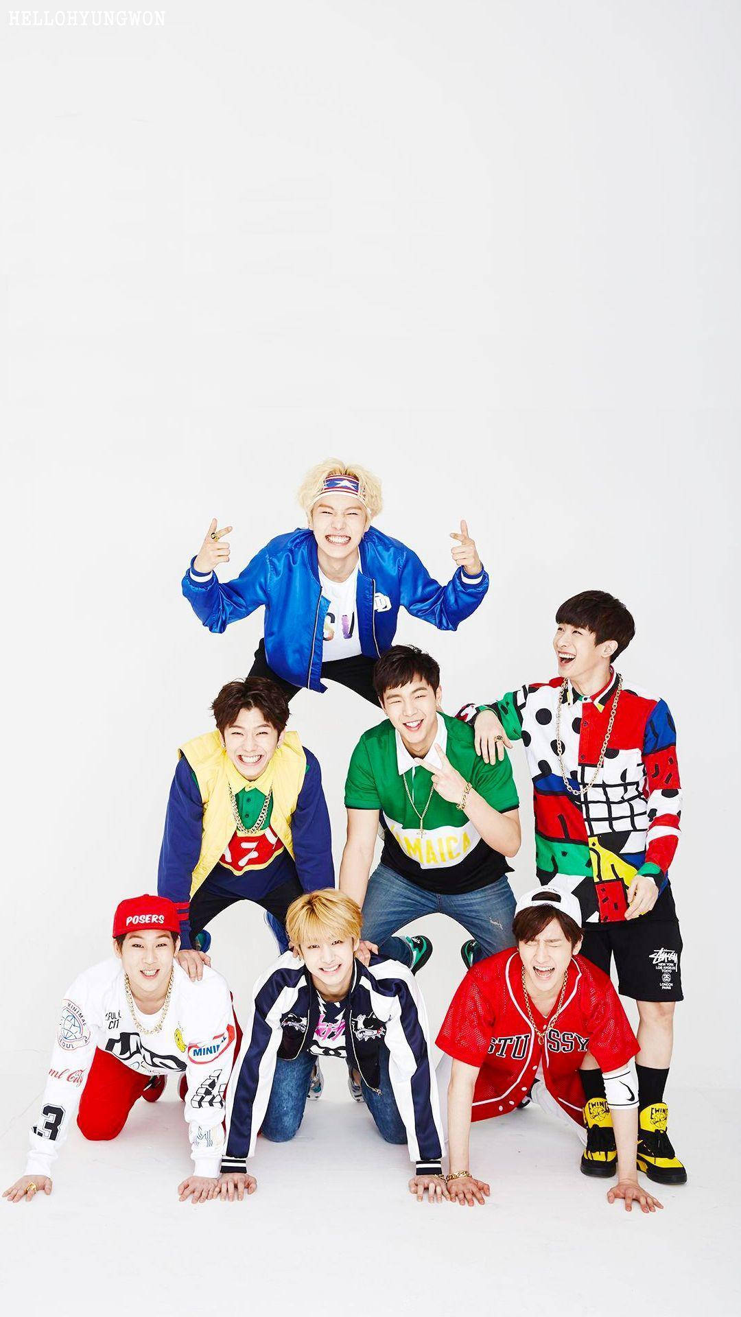 MONSTA X人體金字塔 壁紙 — 七位微笑的年輕男子身穿色彩繽紛的街頭服飾，在純白背景前以金字塔隊形充滿活力地擺姿勢。