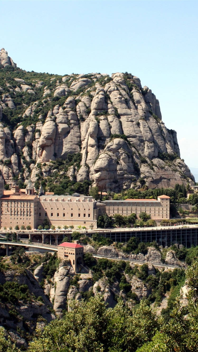 Montserrat 城市手機壁紙 壁紙 — 一座宏偉的修道院依附在蒙特塞拉特山崎嶇的懸崖上，天空清澈湛藍。