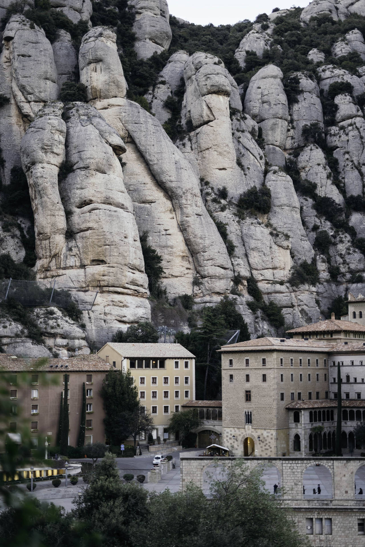 Montserrat 白色巨石 壁紙 — 古老石建築坐落於高聳崎嶇、覆蓋稀疏綠意的石灰岩懸崖腳下。