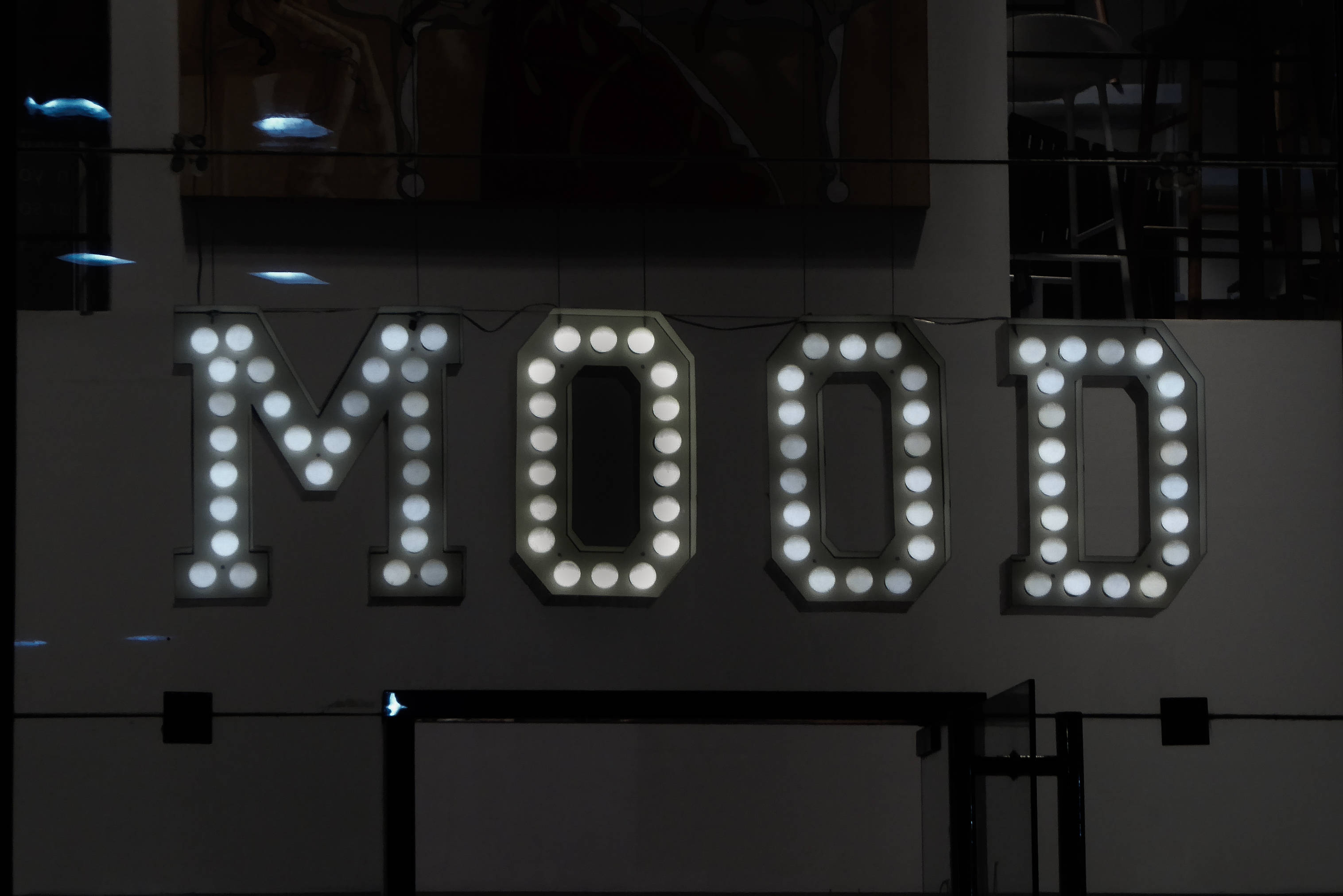 「MOOD」燈光字體 壁紙 — 夜間在黑暗的城市牆上，一個發光的白色帳篷標誌用圓形燈泡拼出MOOD。