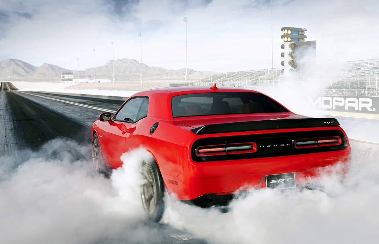紅色 Dodge Challenger SRT 在直線加速賽道上進行燒胎，冒出煙霧。