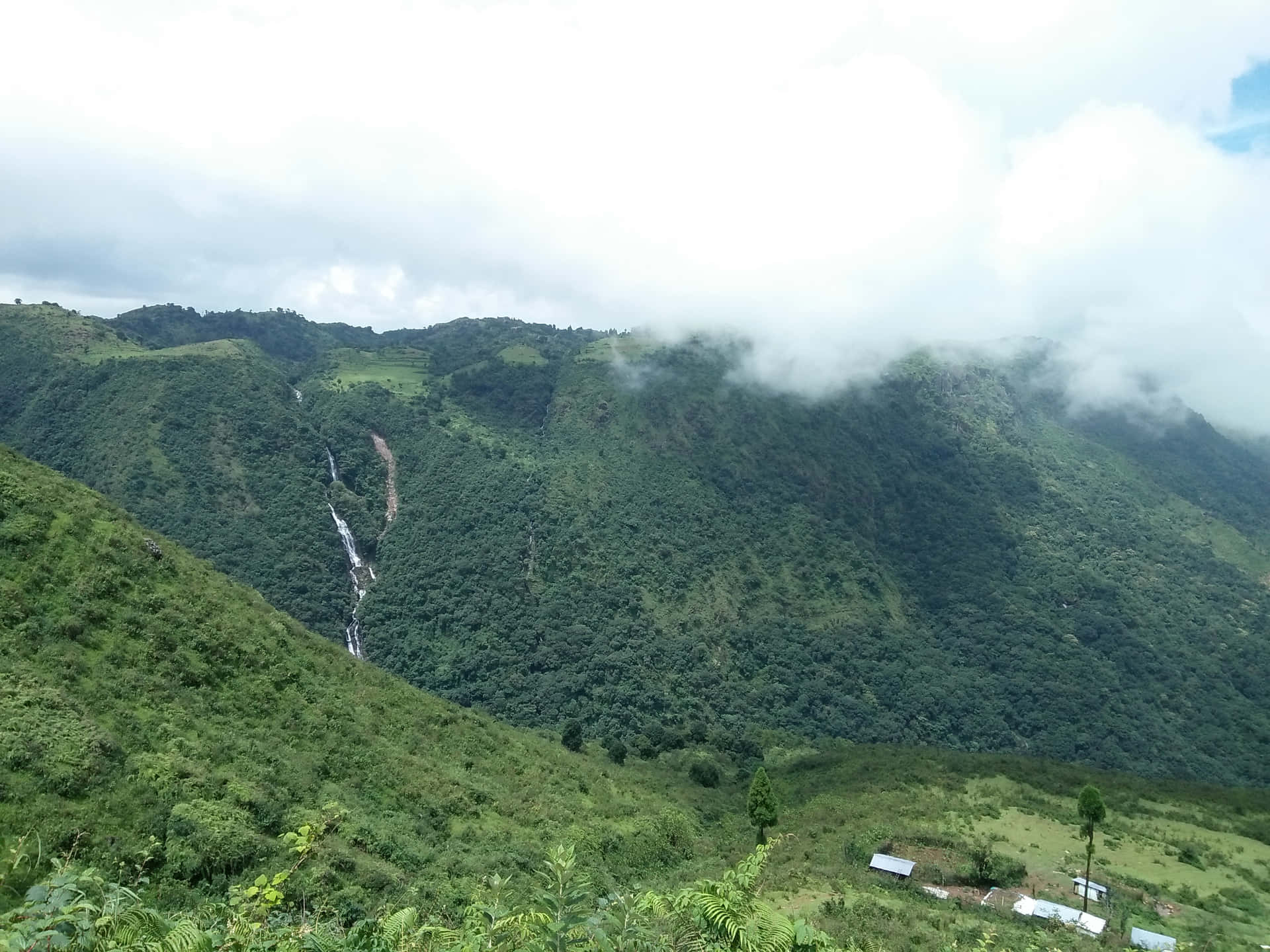 瀑布流下綠色山谷，上方有雲霧飄動，下方有一個小村莊。