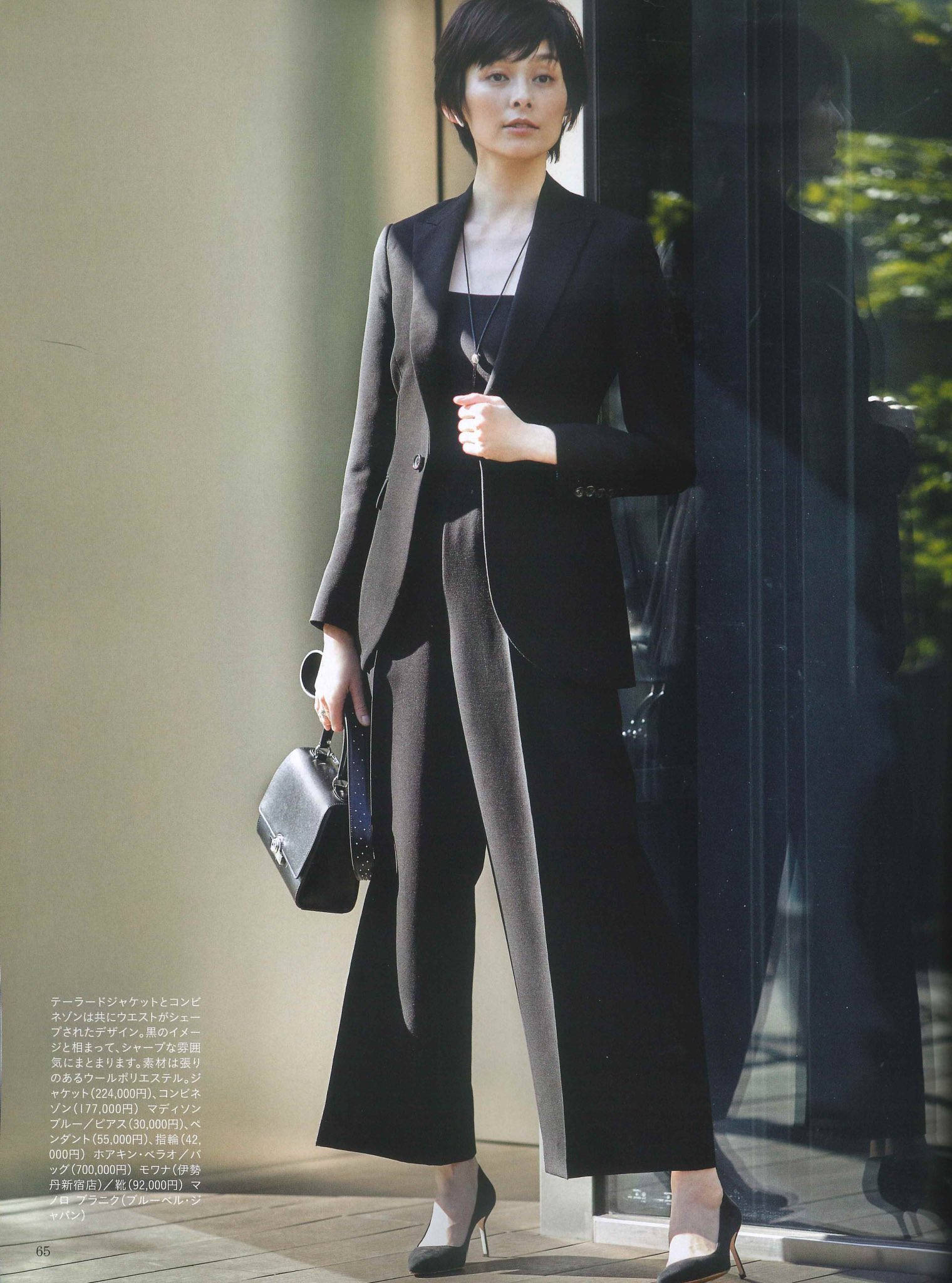 Moynat | 經典時尚之選 壁紙 — 一位優雅的女士身穿時尚黑色西裝，站在玻璃門旁，身後映照著綠意。